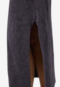 Tmavo šedá sukňa vyrobená z mäkkej, textúrovanej tkaniny má bočný rozparok a rovný strih, čo zaisťuje uvoľnený strih s minimálnymi detailmi.