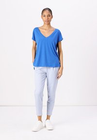T-shirt blu a scollo a V con maniche corte, abbinato a pantaloni tapered azzurri chiari e scarpe bianche. Il tessuto sembra morbido e leggero.