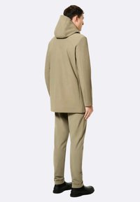 Beige gewatteerde jas met capuchon, een ontspannen pasvorm, lange mouwen en strakke lijnen. Gecombineerd met bijpassende taps toelopende broek en zwarte schoenen.