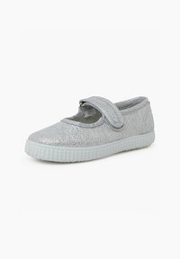 Chaussure en tissu à paillettes argentées avec un bout rond, une sangle en velcro et une semelle blanche texturée ; conception légère et flexible pour un port facile.