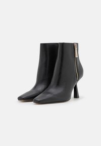 Botines de cuero negro con punta puntiaguda, cremallera lateral y tacón delgado. Textura suave y diseño minimalista.