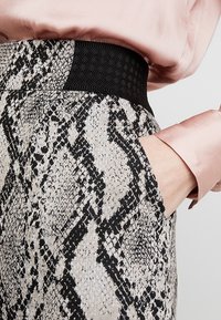 Pantalons à imprimé serpent avec une taille élastique noire, une texture douce et des poches latérales. Le design comprend des nuances de beige et de noir.