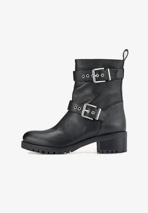 Bottine en cuir noir avec deux brides réglables à boucles, surface texturée, bout rond et talon épais en caoutchouc avec semelle crantée.