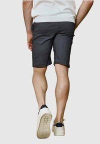 Shorts gris en tissu léger, se terminant au-dessus des genoux. Portés avec des chaussures blanches avec un accent noir. Jambes musclées visibles.