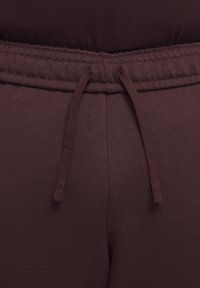 Burgundyröda träningbyxor med en strukturerad yta, utrustade med dragsko i midjan och sydda detaljer som betonar komfort och passform.