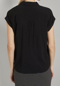 Donna che indossa una blusa nera a maniche corte con risvolti e una gonna a righe bianco e nere, vista di spalle.