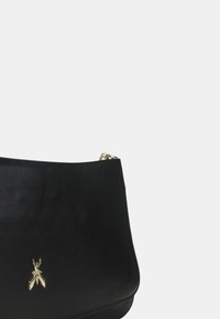 Borsa a mano in pelle nera con una texture liscia, caratterizzata da un accento dorato a forma di charm. Il design è strutturato con una forma arrotondata e una tracolla a catena.