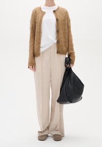 Gebreid vest in warm bruin met een gestructureerd patroon, gecombineerd met lichtbeige broek met wijd uitlopende pijpen en een zwarte leren slouchy tas.