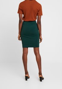 Donkergroene kokerrok van rekbaar materiaal, aansluitend ontwerp, met een naadloze taille, gecombineerd met een geribbelde bruine top met korte mouwen.