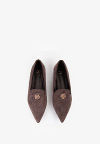 Scarpe in suede marrone con punta affusolata, caratterizzate da un motivo cucito e un bottone decorativo in tonalità oro sulla parte anteriore. Fodera interna liscia.