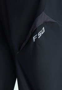 Czarne spodnie sportowe z fakturowaną szaro-srebrną wstawką. Projekt zawiera wyraźne logo "F50" w srebrnym kolorze blisko szwu.