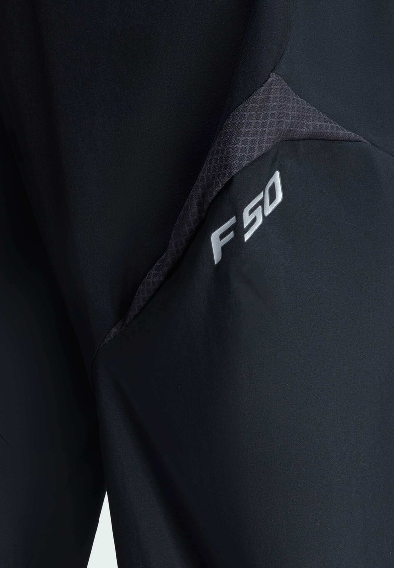 Svarta träningsbyxor med en texturerad grå panel. Designen inkluderar en framträdande "F50"-logotyp i silver nära sömmen.