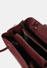 Sac à main en cuir bordeaux avec deux compartiments principaux, une poche centrale zippée et un détail en cuir noué à l'intérieur.