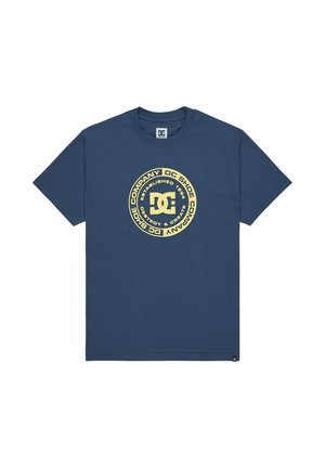 Námornícky modré bavlnené tričko s veľkým kruhovým grafickým motívom v zlatej farbe, obsahujúce text a logo DC Shoes. Krátke rukávy a dizajn s okrúhlym výstrihom.