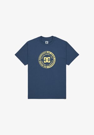 Námornícky modré bavlnené tričko s veľkým kruhovým grafickým motívom v zlatej farbe, obsahujúce text a logo DC Shoes. Krátke rukávy a dizajn s okrúhlym výstrihom.