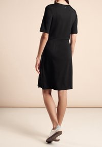 Černé šaty s krátkým rukávem, s přiléhavým korzetem a rozšířenou sukní. Hladká textura, do kolen, kombinované s bílými botami se světle modrými akcenty.