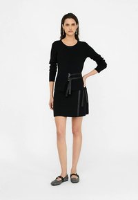 Mustast kootud kampsunist pika varrukaga, millele on kombineeritud must seelik nahast detailide ja vööga taljes.