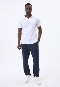 Camisa polo blanca con un patrón texturizado, pantalones sueltos azul marino y zapatillas blancas. El conjunto presenta un diseño casual y relajado.