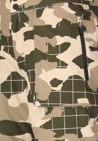 Stoffen voor camouflage-gepatenteerde broeken in verschillende tinten beige en groen met een rasterontwerp. Inclusief een ritszak en een knoopsluiting.
