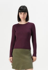 Pull à manches longues côtelé en violet profond, associé à une jupe en velours côtelé olive de longueur genou avec un motif de couture diagonal.