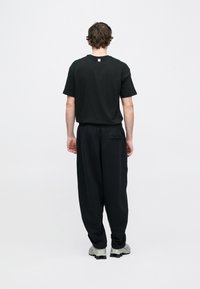 Μαύρο βαμβακερό μπλουζάκι με στρογγυλή λαιμόκοψη και μαύρη άνετη φόρμα με ελαστική μέση και πίσω τσέπη, φορεμένα με γκρι αθλητικά παπούτσια.