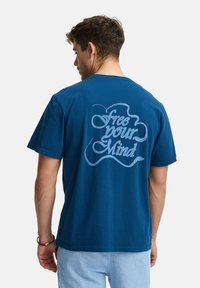 Camiseta de algodón azul marino con un gran gráfico de texto en azul claro en la espalda que dice "libera tu mente". Mangas cortas, diseño de cuello redondo.