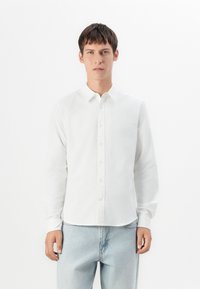 Witte overhemd met lange mouwen en knoopsluiting, gemaakt van een gladde, lichte stof met een klassieke kraag en rechte pasvorm. Eenvoudig ontwerp, minimale details.