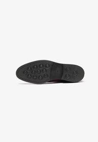 Suela de zapato de goma negra con patrones de tracción circulares, superficie ligeramente texturizada y borde curvado para un ajuste ergonómico.