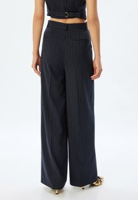 Pantalons à jambes larges en bleu marine foncé avec des rayures contrastantes. Comprend des poches arrière et une taille structurée. Tissu lisse avec une coupe ajustée.