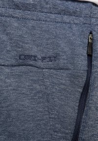 Tejido Dri-FIT azul con acabado texturizado, que cuenta con un bolsillo con cremallera y un logotipo bordado, mostrando una combinación de estilo y funcionalidad.