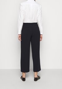 Donkerblauwe wijde broek van gladde stof, met een middelhoge taille en twee achterzakken, gestyled met een witte overhemd met knopen.
