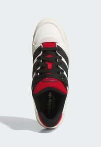 White and black athletic shoe with red mesh accents, featuring black laces, three black stripes on the side, and a padded collar.