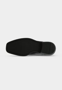 Semelle de chaussure habillée en cuir noir avec un bout carré et un talon segmenté, présentée sur fond blanc.