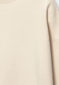 Jasno beżowy sweatshirt z miękkiego, teksturowanego materiału. Charakteryzuje się prążkowanym dekoltem i opuszczonymi szwami ramion, co zapewnia luźny krój.