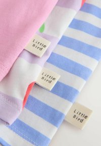 Tres prendas de bebé dobladas con etiquetas "Little Bird", con patrones de flores rosa y pastel, y rayas azules y blancas.
