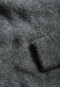 Grå uldstof med en blød, struktureret overflade og et let fuzzy udseende. Har et enkelt, sømløst design uden synlige mønstre.