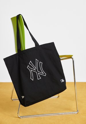 Black tote bag with white New York Yankees logo hanging on lime green chair with chrome legs, set on mustard floor.
