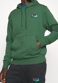 Zelená mikina s kapucí z bavlněné směsi, s přední kapsou, stahovací kapucí a vícebarevným logem Nike na hrudi.
