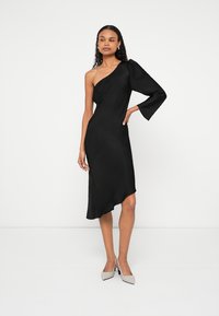 Čierne asymetrické šaty s jedným ramienkom z hladkej látky; majú asymetrický lem a nafúknutý dlhý rukáv. Nosené s svetlými vysokými podpätkami.