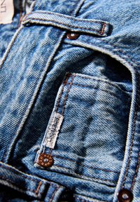 Giacca di denim color azzurro chiaro, con cuciture marroni e un'etichetta vintage. Include una tasca frontale e chiusure con bottoni.