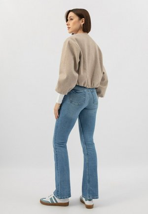 Pull court beige avec des manches bouffantes, associé à un jean évasé bleu et des baskets blanches avec des rayures teal, vu de dos.