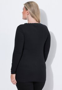 Schwarzes langärmliges Oberteil mit gerippter Textur, Rundhalsausschnitt und gewelltem Detail am Rücken, kombiniert mit schwarzen Hosen.