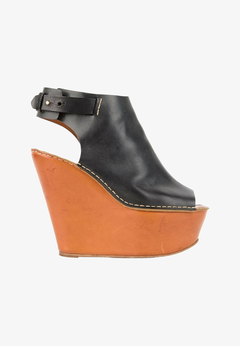 Sandale compensée en cuir noir à bout ouvert avec semelle plateforme épaisse marron et fermeture à boucle à la bride de cheville sur fond blanc.