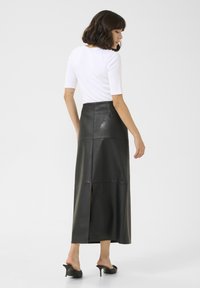Falda larga de cuero negro con una abertura, que presenta una cintura ajustada y detalles de panel. Combinada con una blusa blanca ajustada y tacones deslizantes.