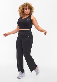 Black athletic crop top with logo, paired with black wide-leg pants featuring a side logo detail. Smooth, stretch fabric; casual fit.