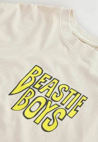 T-shirt blanc avec un logo texte "BEASTIE BOYS" jaune et noir centré sur le devant.