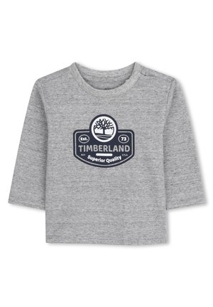 Chemise à manches longues grise en matériau doux, ornée d'un logo circulaire Timberland en bleu marine, avec le texte "Qualité Supérieure" et "Est. 73" en dessous.