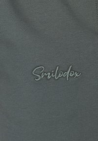 Grå athletic stof med en blød tekstur har et broderet "Smilodox" logo i en kontrasterende lys grå.