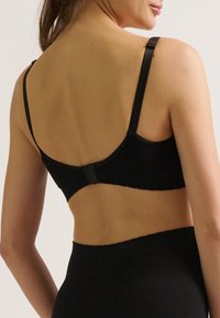 Soutien-gorge noir à côtes avec bretelles réglables et fermeture à crochets. Présente une texture lisse et un design minimaliste, montrant le dos.