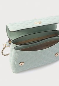 Geantă matlasată verde mentă cu un cârlig auriu și o curea cu lanț. Interiorul are două compartimente și o căptușeală cu marcă.